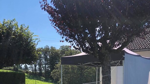 An outdoor seating area with two chairs and a table under a canopy, surrounded by greenery and a small shed. - APARTMENT IN HOUSE (Lacapelle-Viescamp)