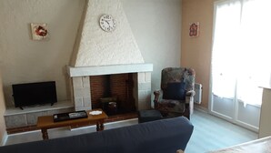 A living room with a fireplace, a television, a sofa, and a chair. - APARTMENT IN HOUSE (Lacapelle-Viescamp)