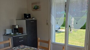 A dining area with a table set for four, a kitchen area with a coffee maker, and a view of a garden through a glass door. - APARTMENT IN HOUSE (Lacapelle-Viescamp)