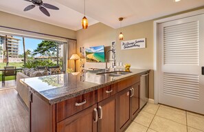 A kitchen with a granite countertop, wooden cabinets, a stainless steel sink, and a ceiling fan.