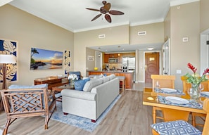 A spacious living room with a sofa, a dining area with a table set for two, and a kitchen in the background.