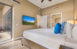 A hotel room with a large bed, a television mounted on the wall, and a sliding glass door leading to an outdoor area. - Maui Resort Rentals: Honua Kai Hokulani 140 – Upgraded Large Ground Floor 1BR, Spacious Lawn Area + Easy Pools/Beach Access (Lahaina)