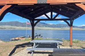 Situated by a serene lake, this pavilion offers a picnic table with a scenic view of the surrounding landscape and mountains.