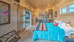 A wooden interior with a bed, a bathroom, and a kitchen area. - Ennis Lake Studio w/ Kayak, Pool & Fire Pit! (McAllister)
