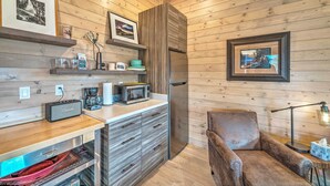A modern kitchen with wooden walls, a built-in microwave, and a refrigerator. There are shelves with decorative items and a chair in the corner. - Ennis Lake Studio w/ Kayak, Pool & Fire Pit! (McAllister)