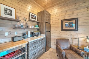 Cozy kitchen area with microwave, refrigerator, and wooden countertop, featuring a comfortable armchair and personal touches.