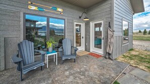 A covered patio with Adirondack chairs, a table, and a door leading to a garage. - Ennis Lake Studio w/ Kayak, Pool & Fire Pit! (McAllister)