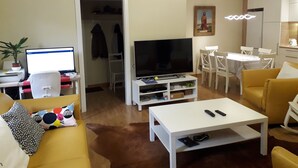 Een woonkamer met een bank, een salontafel, een televisie en een eethoek met stoelen en een tafel.