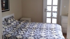 Een slaapkamer met een bed, een nachtkastje, een deur met ramen en een lijst met een foto aan de muur.