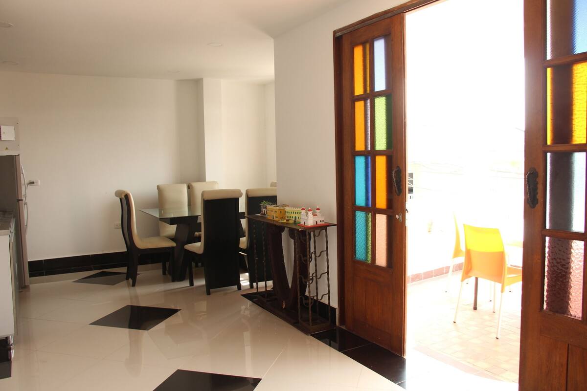 A dining area with a table and chairs, a small table with items, and a door with colorful glass panels.