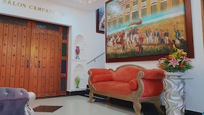 A salon with a wooden door, a red sofa, and a painting of a historical scene. - Hotel Boutique Campanario del Río (Soledad)