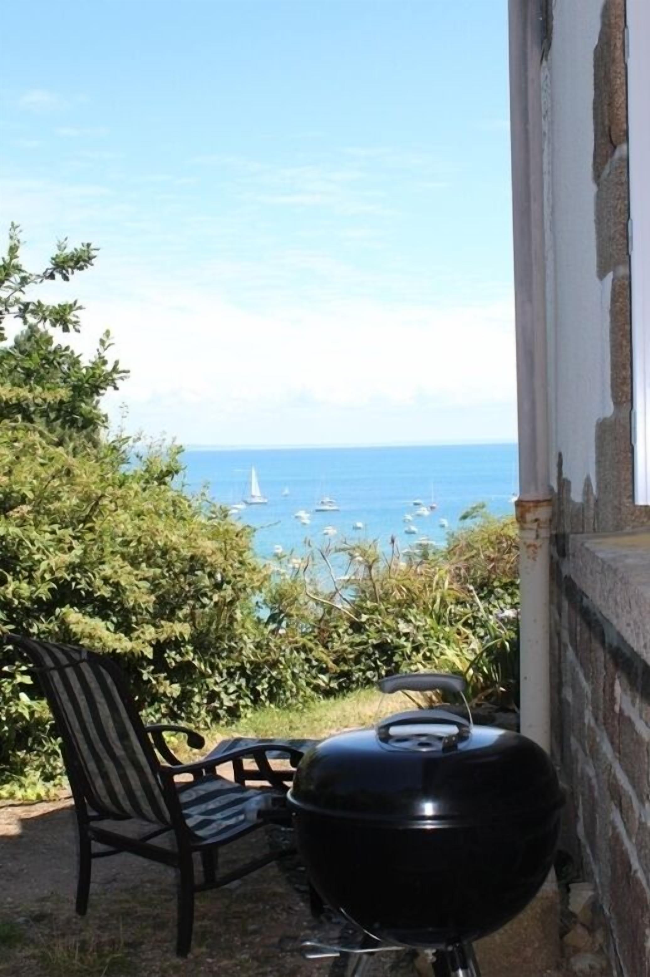 A patio with a grill and a chair overlooking a sea view with boats.