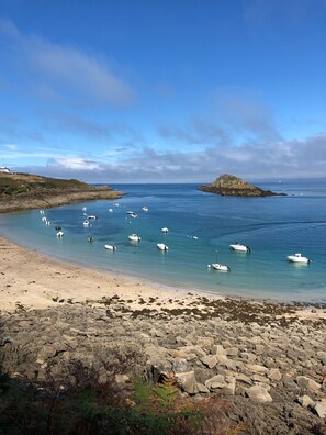 A rocky beach with boats anchored in calm waters, a lighthouse in the distance, and a small island.