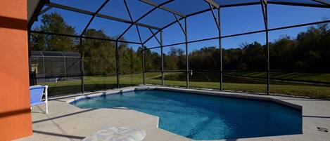 A covered outdoor swimming pool with lounge chairs and a view of a green landscape.