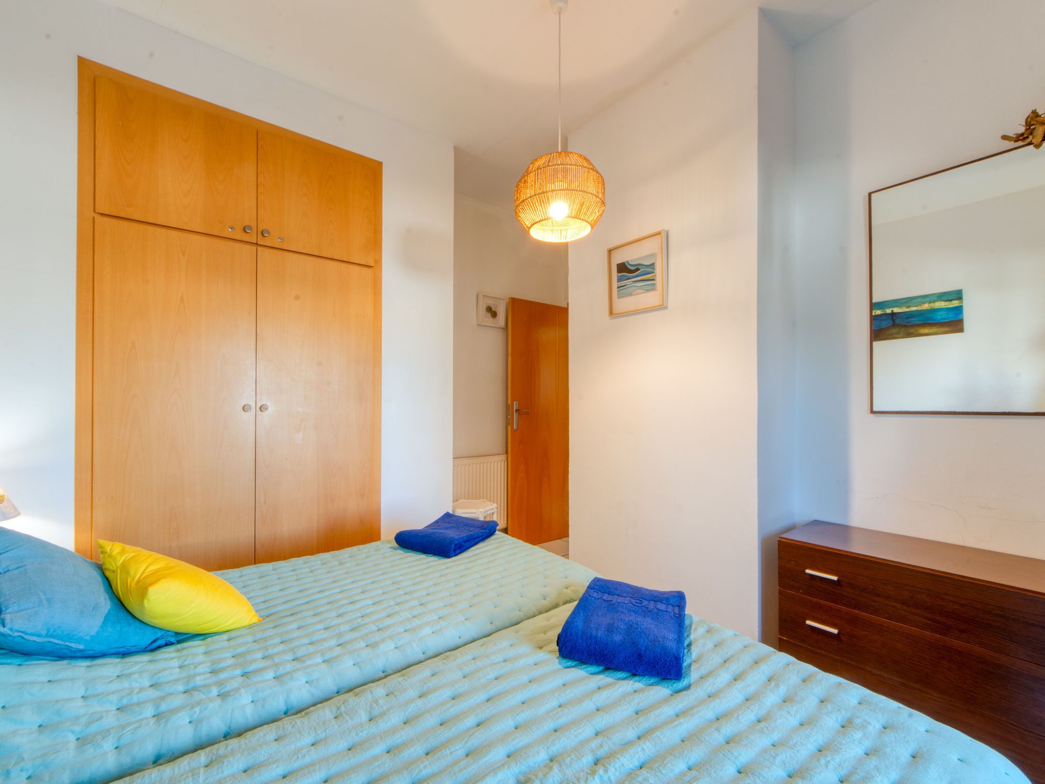 Un dormitorio con cama, armario, lámpara colgante y un cuadro en la pared.
