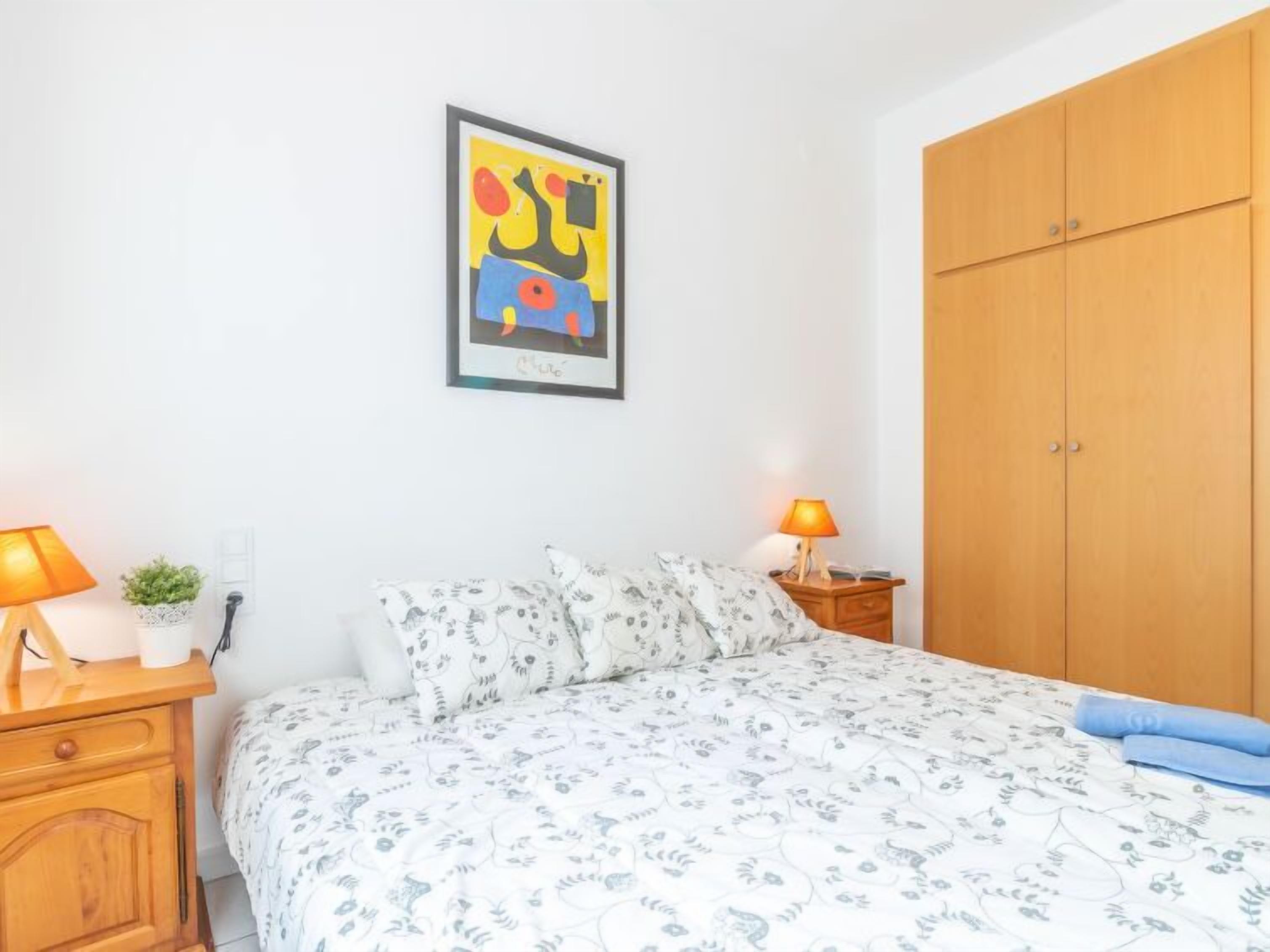 Ein Schlafzimmer mit einem Bett, zwei Nachttischen mit Lampen, einem Kleiderschrank und einem gerahmten Bild an der Wand.