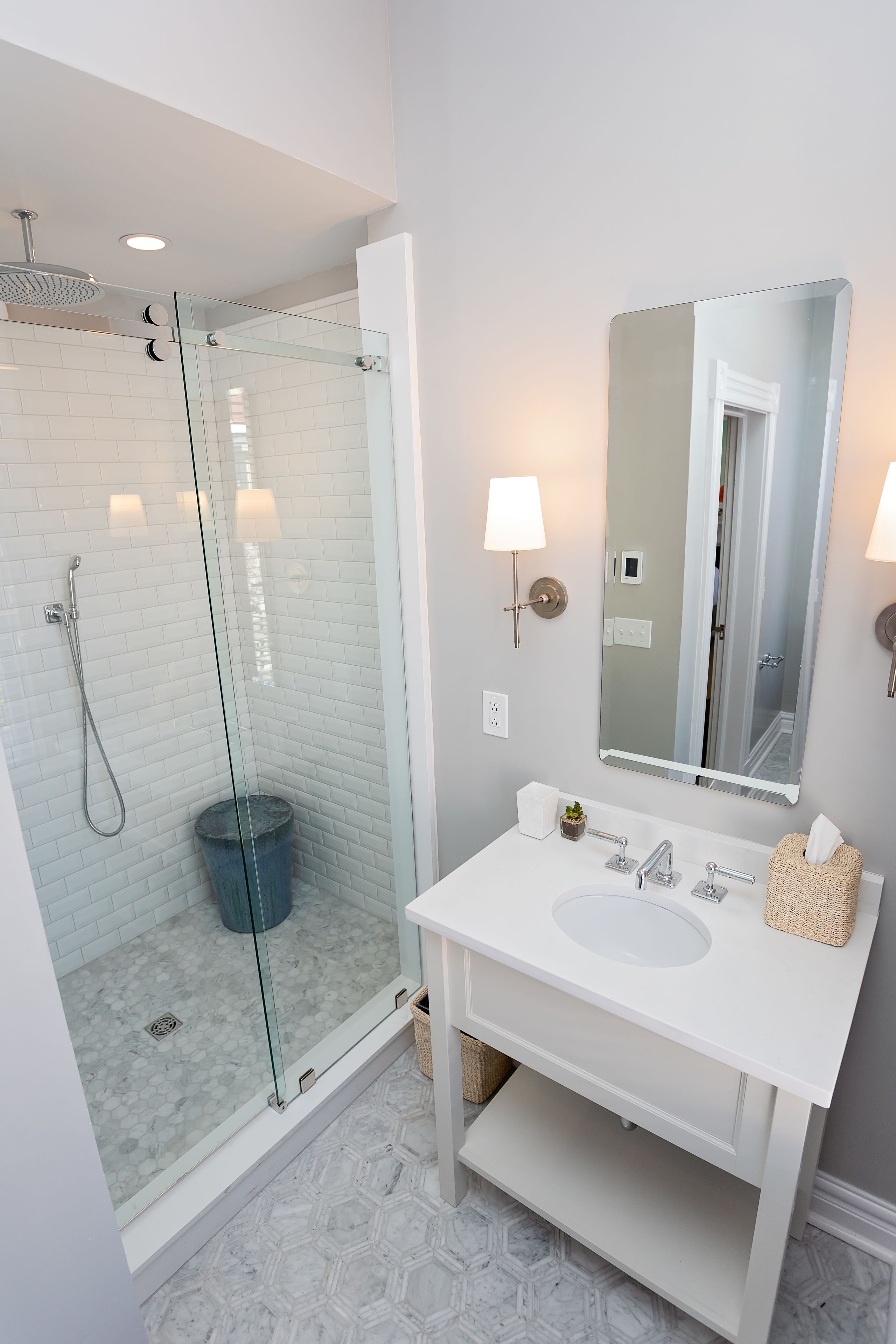Un baño moderno con ducha de vidrio, lavamanos blanco y un espejo grande.