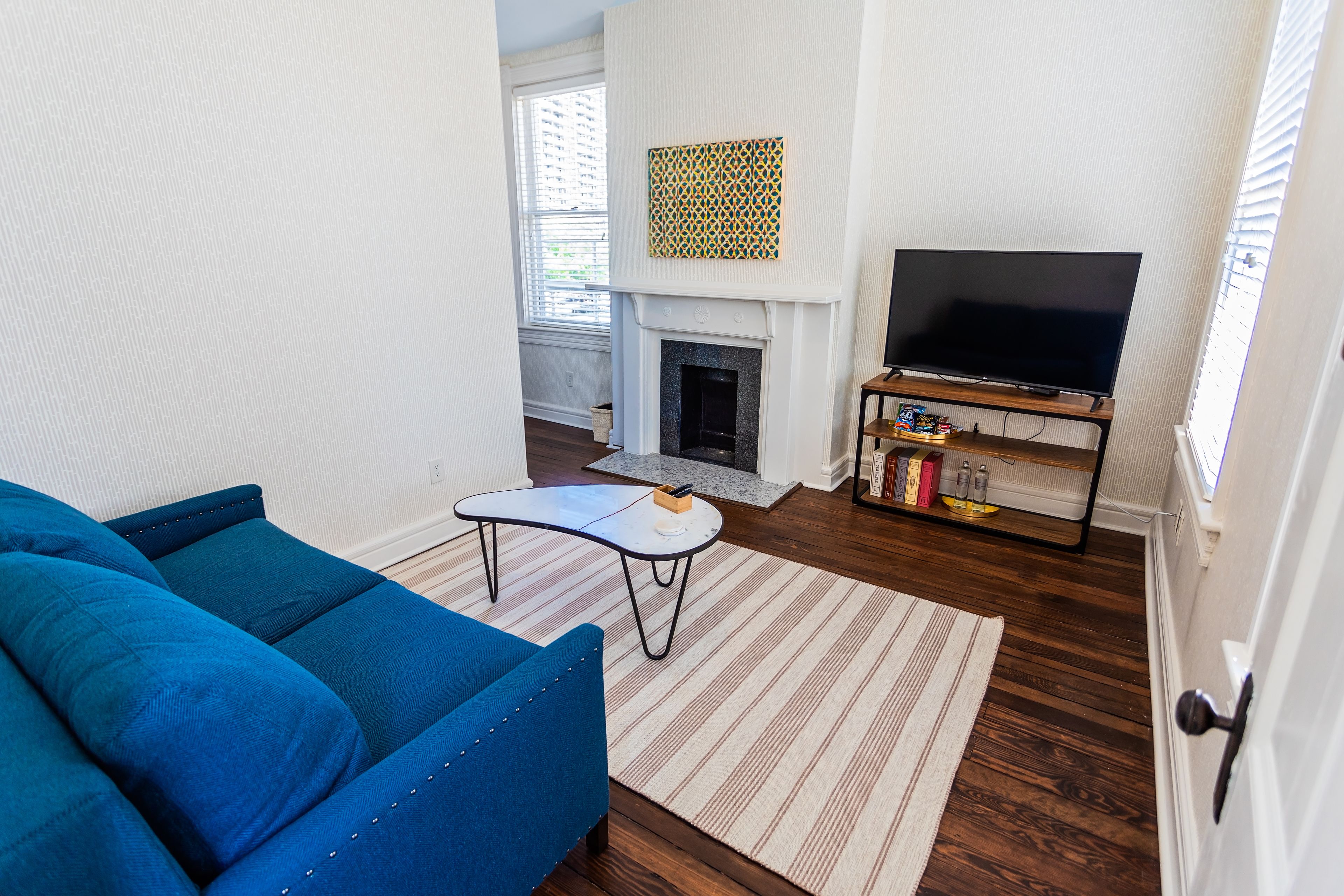 A living room with a blue sofa, a fireplace, a television on a wooden stand, and a patterned wall hanging.