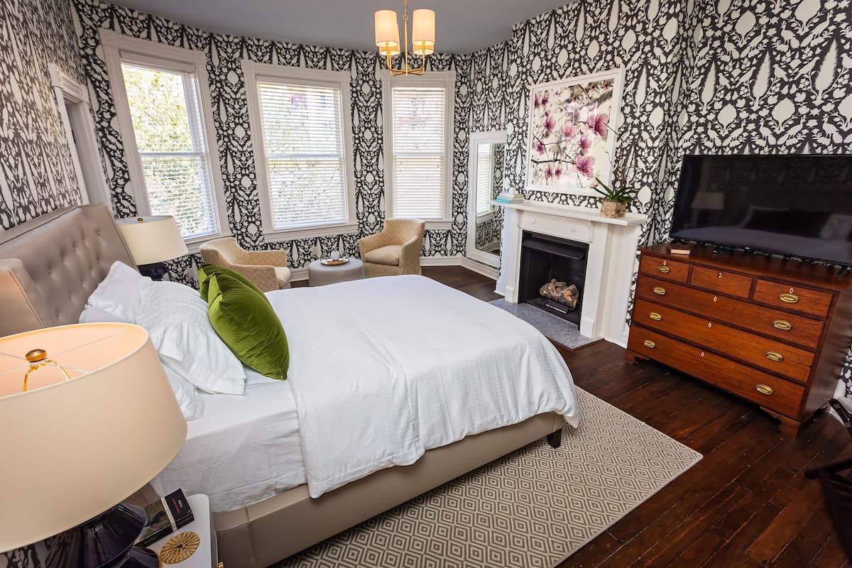 A bedroom with a large bed, a dresser, a TV, and a fireplace.