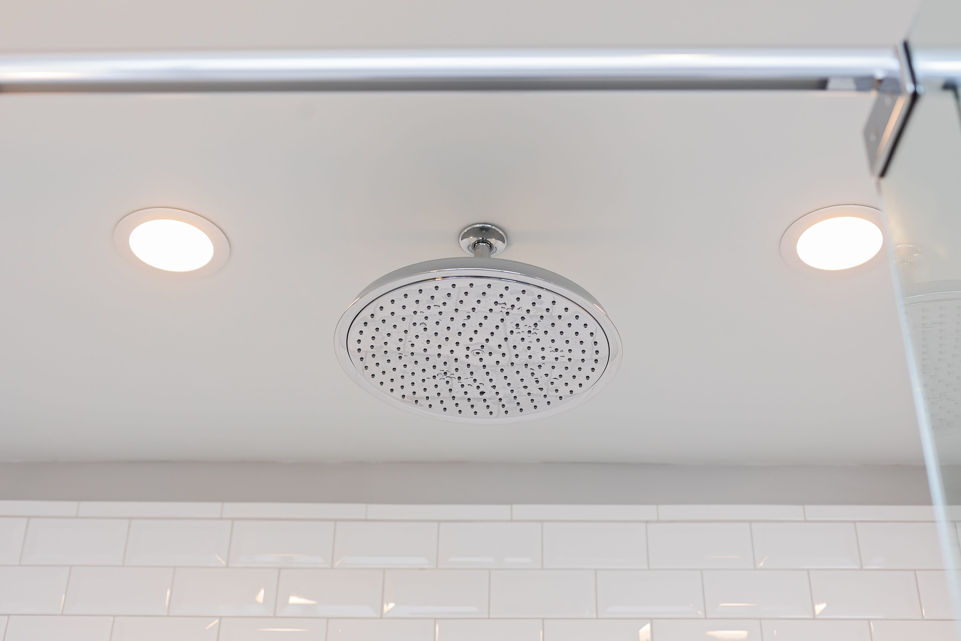 A modern bathroom with a round showerhead, white tiles, and a chrome shower bar.