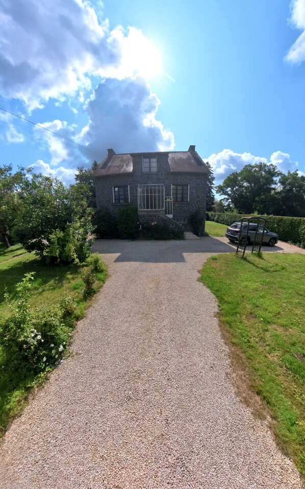 A stone house with a gravel driveway leading to a gated entrance.