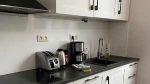 Une cuisine moderne avec des meubles blancs, un plan de travail noir, une machine à café, un grille-pain et un évier.