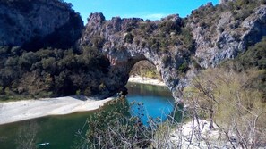 Une arche naturelle formée par la roche, enjambant une rivière et entourée d’une forêt.
