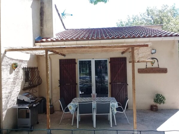 Une terrasse extérieure avec une table et des chaises, un barbecue et un espace salon abrité.
