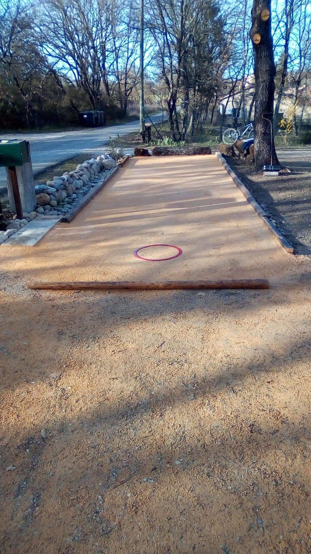 Ein Shuffleboard-Tisch mit einer Holzumrandung, einem roten Kreis in der Mitte und einer Kiesfläche.