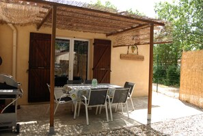 Une terrasse extérieure avec une table et des chaises, un barbecue et une pergola.