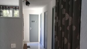 A hallway with a tiled floor, a door labeled "TOILET", and a window with curtains.