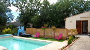 A swimming pool with a wooden deck, pink chairs, and a wooden fence.