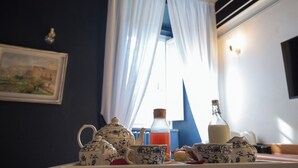 A table set with a teapot, cups, a bottle, and pastries in a room with a window and curtains. - Villa Klaudia - charming house_ Pompeii (San Giorgio a Cremano)