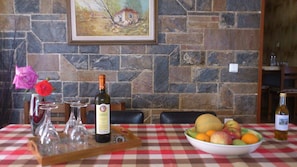 A dining table with a checkered tablecloth, a bottle of wine, a bowl of fruit, and a painting on the wall.