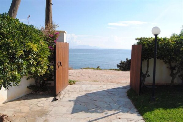 A stone pathway leading to a wooden gate with a view of the sea.