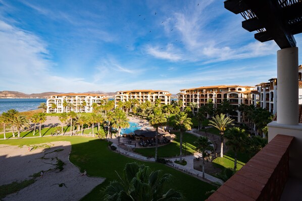 A resort with multiple buildings, a swimming pool, palm trees, and a beach.