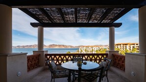 Un espacio de estar al aire libre cubierto con mesa y sillas, con vistas a una playa y montañas.
