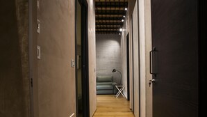 Un pasillo estrecho con suelo de madera, una puerta oscura a la derecha y un sofá al fondo.