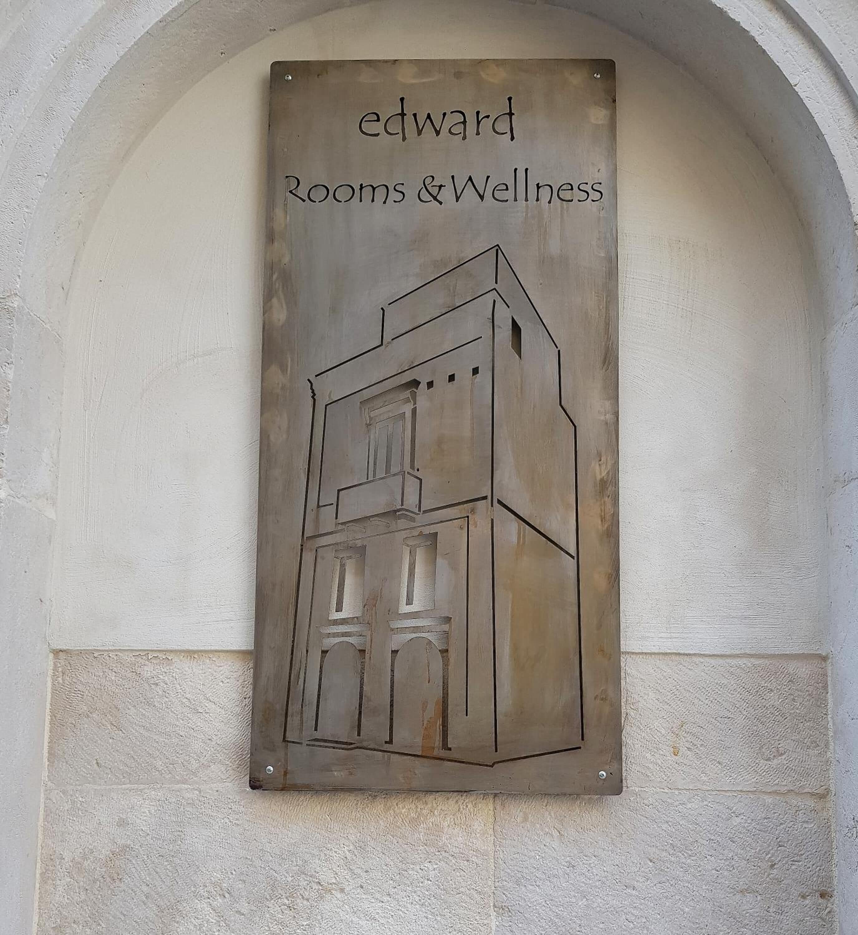 Et skilt med en bygningskontur og teksten 'Edward Rooms & Wellness'.