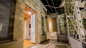 Un espacio exterior bien iluminado con suelo de madera, una silla plegable y una pared blanca con una ventana.