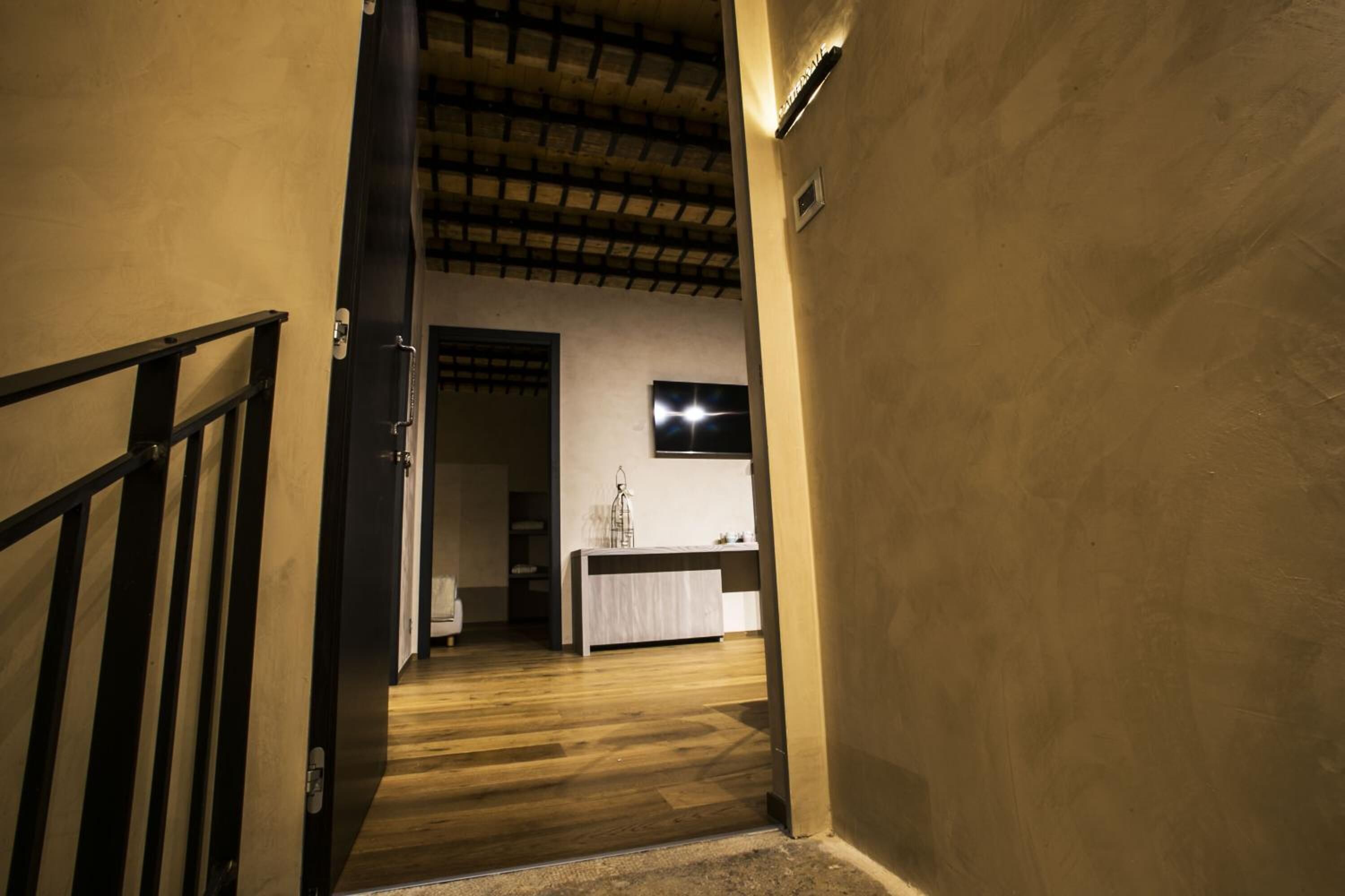 A hallway with wooden flooring, a black railing on the left, and a white wall with a mounted picture frame.