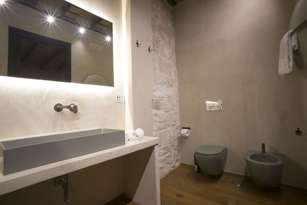 A modern bathroom with a large sink, a stone accent wall, a toilet, and a bidet.