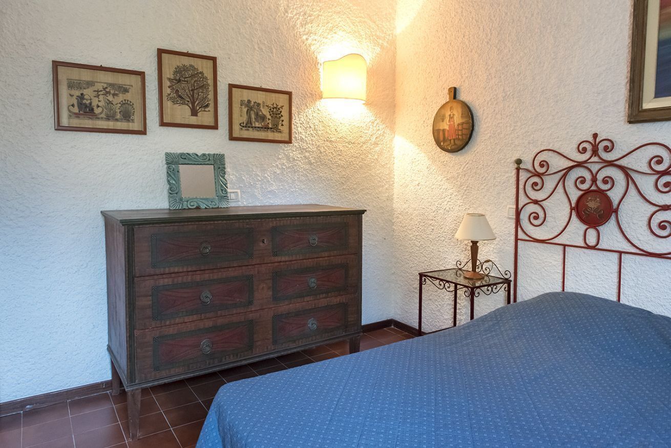 A bedroom with a bed, dresser, wall-mounted light, and framed pictures.