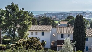 Un quartier résidentiel en bord de mer, avec des bâtiments blancs, une vue sur la mer et un grand arbre imposant qui se distingue.