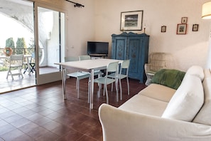 A living room with a sofa, a dining table with chairs, a television, a cabinet, and a balcony with a view.