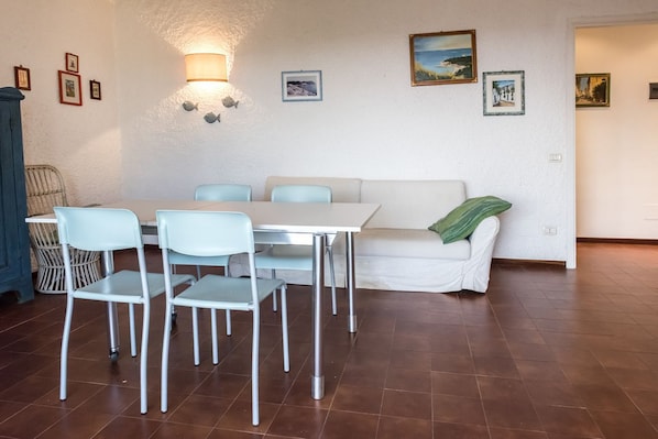 A dining area with a white table and chairs, a white sofa with a green throw, and wall-mounted pictures.