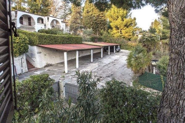 Un espacio exterior cubierto con suelo de hormigón, rodeado de follaje y un edificio con ventanas de arco.