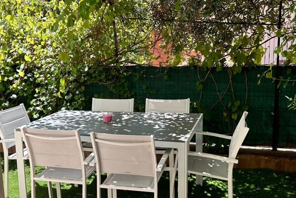 An outdoor patio with a table and chairs, surrounded by greenery.