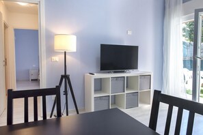 A room with a TV on a white stand, a lamp, and a table with chairs.