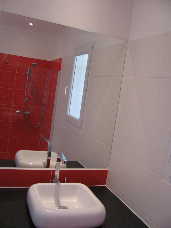 A bathroom with a white sink, a shower with a red wall, and a window. - Villa le Cyprès for 4 pers (Montagnac)